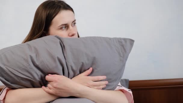 不幸な若い女性はベッドの上に座って 落ち込んで感じて 悪い関係やブレークアップについて考えて 動揺した女の子は 心理的なトラブルに苦しんで孤独感 灰色の枕を包含する — ストック動画