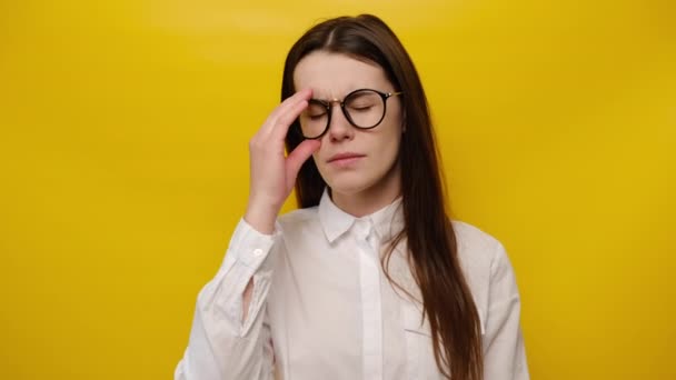 疲れた若い女性がメガネを脱いで疲れたマッサージ鼻橋に触れ 疲れ果てた少女は頭痛に苦しみ 痛みを感じ 心を落ち着かせ ストレス解消の概念は 黄色の背景に隔離された — ストック動画