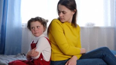 Kızgın genç anne ve küçük kız, gri yatakta sırt sırta oturuyorlar, konuşmuyorlar, inatçı küçük kız ve annenin birbirini görmezden gelmesi rahatsız ediyor, çocuklu ebeveynler fikir ayrılıkları yaşıyor.