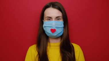 Coronavirus konsepti. Hastalıkla mücadelede yardım ettikleri için doktorlara ve hemşirelere şükranlarını göstermek amacıyla üzerinde kalp olan bir sağlık maskesi takan kızı alkışlayın. Covid 19