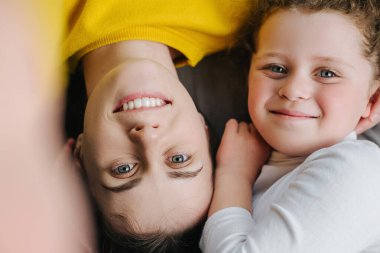 Anne ve küçük kızın rahat yatak odasında rahatlaması. Neşeli anne ve küçük kızı yatağa uzanmış kameraya bakıp gülümsüyor ve mutlu selfie çekiyorlar.