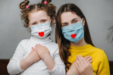 Anneler ve kızlar ellerini göğüslerine koyup yatağa otururlar, hastalıkla mücadelede doktorlara ve hemşirelere şükranlarını göstermek için yüzlerine kalp maskesi takarlar. Covid 19