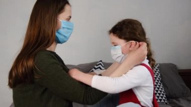 Kızının virüs maskesi takmasına yardım eden, evdeki yatakta oturan, ailesini bulaşıcı hastalıklardan korumaya çalışan bir anne. Koronavirüs veya COVID-19 salgın hastalık belirtileri