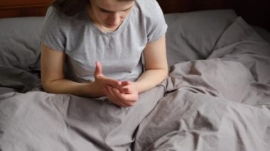 Yatakta oturan yorgun genç bir kadın romatizma eklem iltihabı olan bir ele masaj yapıyor, bileğe dokunan bir kız eklem ağrısı çekiyor osteoartrit hastalığı olan bir eklem ağrısı.