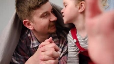 Neşeli pozitif baba ve kız, battaniyeyle kaplı olarak yatağa uzanmış kameraya bakıyor, çocuklu babaya gülümsüyor, video görüşmesi yapıyor, aile video blogcuları video blogu ya da video bloğu kaydediyor.