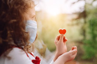 Pencere kenarında oturan küçük bir kız, elinde küçük kırmızı bir kalple Coronavirus COVID-19 salgını sırasında hastanede çalışan hemşirelere ve sağlık çalışanlarına teşekkür etmenin bir yolunu buluyor. Seçici odak