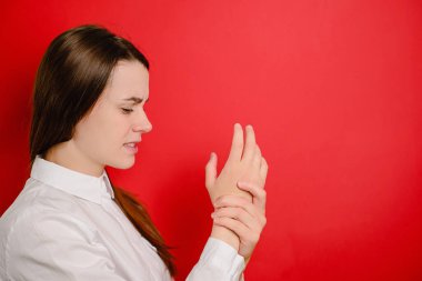 El ya da bilek ağrısı çeken, kırmızı arka planda izole edilmiş, bileğe dokunan, eklem ağrısı çeken, osteoartrit hastalığı olan mutsuz bir kadın. Ofis sendromu