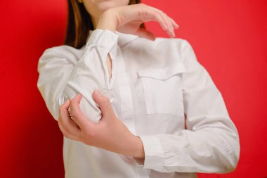 Beyaz tişörtlü, kırmızı stüdyo arka planında kronik eklem romatizmasından muzdarip genç bir kadının görüntüsü. Dirsek ağrısı ve tedavi kavramı. Seçici odak