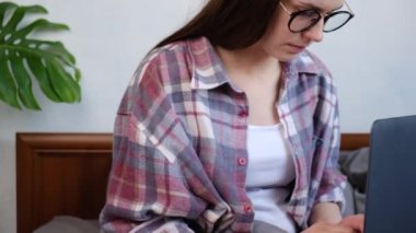 Gözlüklerini çıkaran üzgün genç bir kadın bilgisayarın dizüstü bilgisayarla aynı yatakta oturmasından bıktı. Mutsuz, yorgun bir kızın uzun dizüstü bilgisayar kullandıktan sonra kuru gözlere masaj yapma sorunu var.