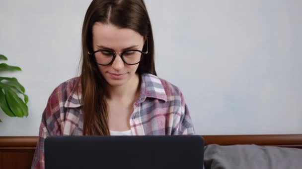 家の居心地の良いベッドに座り女性従業員がビジネス戦略を考え問題を解決するためにノートパソコンを使って財務報告書を作成しました — ストック動画