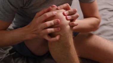 Yatakta oturan, dizine elleriyle dokunan, acıyı hisseden, tanınamayan genç adamı yakından çek. Adamın bacağı ağrıyor, kendini iyi hissetmiyor, sağlık sorunu kavramı, osteoartrit.