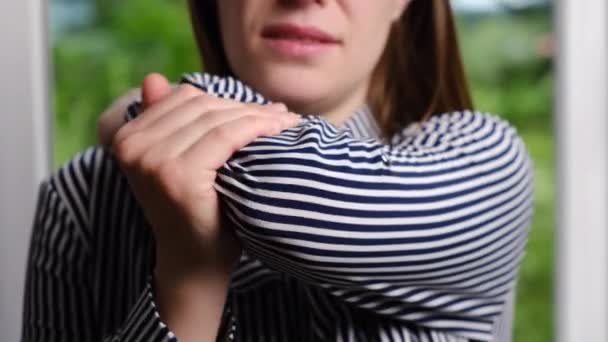 負傷した肘を持つウィンドウの近くに立ってシャツの疲れ不幸な若い女性のクローズアップは 関節痛を緩和するためにマッサージを行います 医療と腕の痛みの概念 選択的焦点 — ストック動画