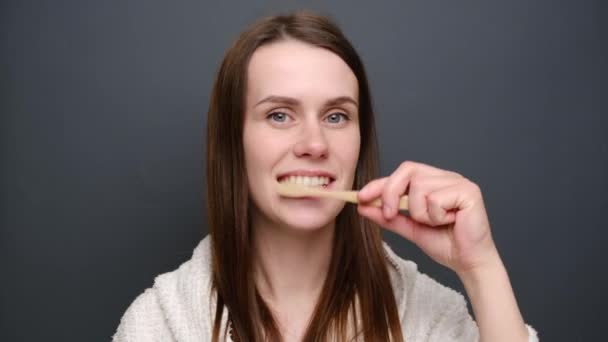 Όμορφη Νεαρή Γυναίκα Βουρτσίζει Δόντια Ξύλινη Οδοντόβουρτσα Φοράει Λευκή Ρόμπα — Αρχείο Βίντεο