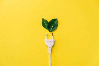 Enerji kavramını sakla. Yaratıcı üst görünüm düz elektrik prizi yatağı, kopyalama alanı olan taze yeşil yapraklar sarı arka planda minimal biçimde