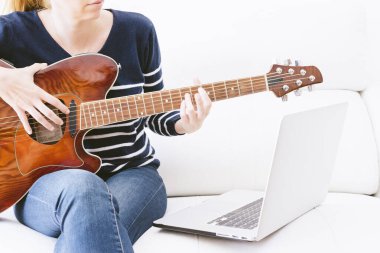 Gitar dersini takip eden genç bir kadın beyaz arka plan fotokopi alanındaki koltukta bilgisayar başında oturuyor. seçici odak