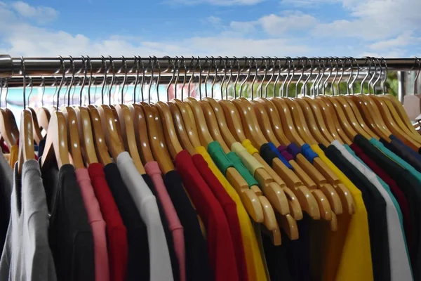 Kleurrijke shirts op houten hangers op markt of winkel achtergrond. — Stockfoto