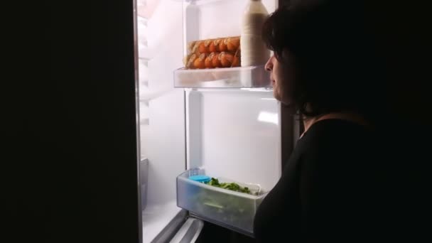 Uma garota faminta abre a geladeira à noite e leva o bolo . — Vídeo de Stock