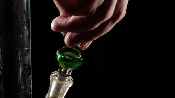 Hand gegossen und tampfen Marihuana in einem Glas bong.on einem schwarzen Hintergrund Nahaufnahme. — Stockvideo