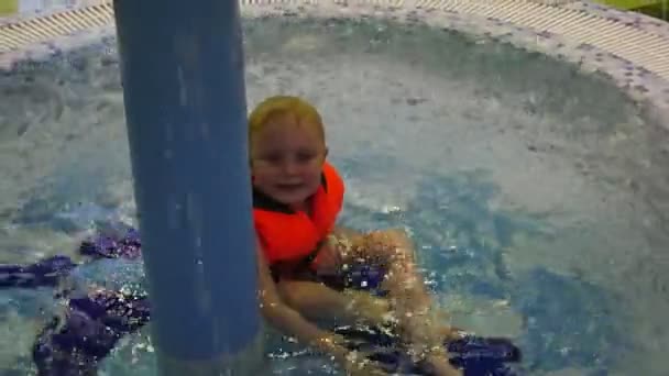 Kleiner Junge in Schwimmweste sitzt im Planschbecken auf tropfendem Wasser. — Stockvideo