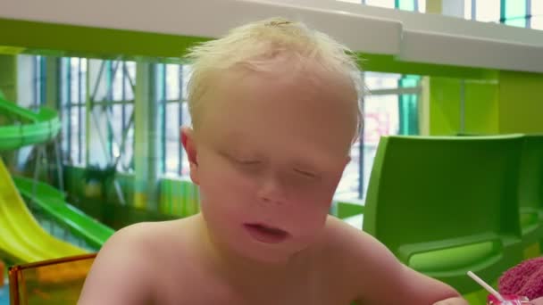 Joli petit garçon aux cheveux blancs assis dans un café, au parc aquatique et parlant . — Video