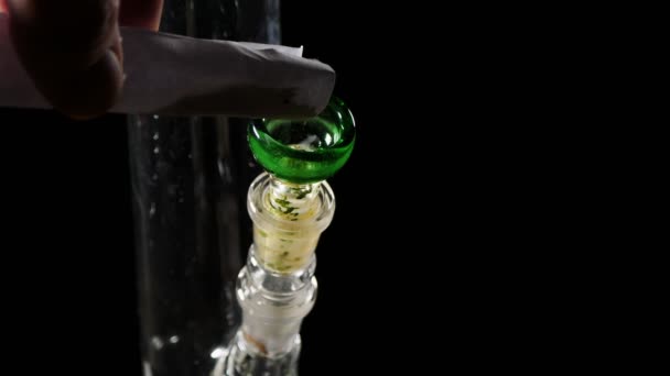 In glazen Bong giet cannabis.Een gedraaid stuk papier wordt marihuana uitgedeeld. — Stockvideo
