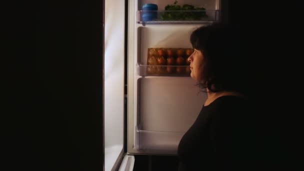 Толстая женщина открывает холодильник ночью и берет пирог. Голод, переедание, диета . — стоковое видео
