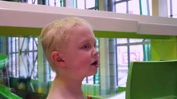 Das Kind im Wasserpark sitzt am Tisch, der Junge mit den blonden Haaren. — Stockvideo