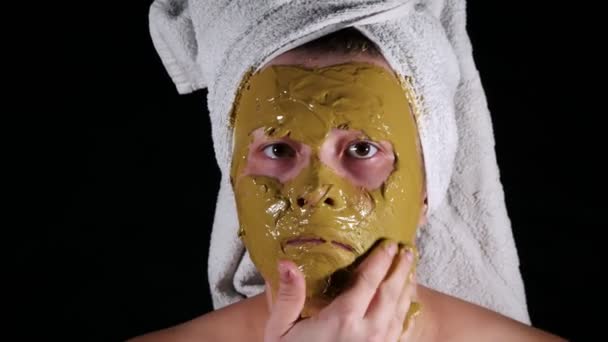 Donna 30 anni con un asciugamano sulla testa provoca una maschera ringiovanente sul viso . — Video Stock