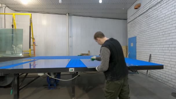 Ein Mann zerschneidet Glasscheiben auf einem blauen Tisch zum Überschneiden. — Stockvideo