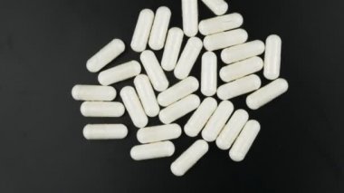 Unrecognizable white capsule with powder inside, rotate on a black background.