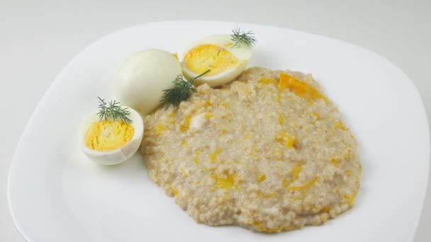 Kaše a dvě vajíčka. Vařený ječmen s dýní a mlékem.Na bílém talíři. — Stock video
