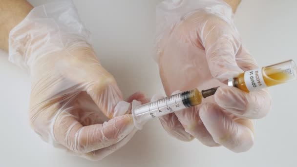 Handen met medische handschoenen met een spuit en een injectieflacon met vaccin van 2019-nCoV. — Stockvideo