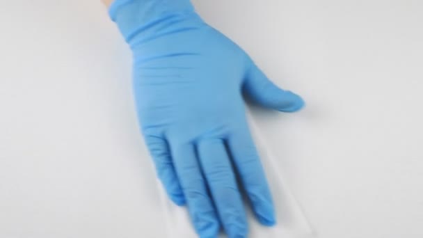 Hand in een blauwe medische handschoen wegwerp doek veegt het witte oppervlak. — Stockvideo