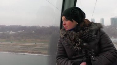 Kadın teleferiğe biner ve pencereden dışarı bakar..