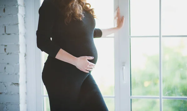 Zbliżenie piękna Pani w ciąży w eleganckim stanowią w czarnej sukni. Portret sexy moda model dziewczyna w bieliźnie w pobliżu okna. Piękno zmysłowe woman z atrakcyjny ciało pomieszczeniu. Zbliżenie kobiet brzuchem — Zdjęcie stockowe
