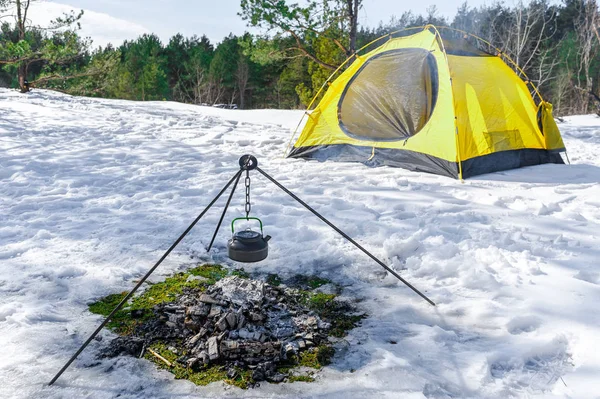 Campfire and tent in wilderness, snow on the ground