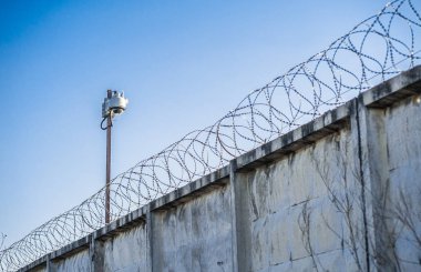 Hapishanede barbwire veya mavi gökyüzü arka plan ile diğer korunan nesne arasında asılı güvenlik kamerası yakından görünümü. Modern denetim yöntemleri. Güvenlik ve güvenlikte yeni teknolojiyi kullanma.