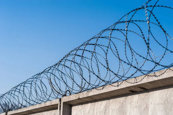 Close up view of security camera hanging among barbwire in prison or other guarded object with blue sky background. Modern ways of supervision. Using new technology in security and safety. — Stock Photo, Image