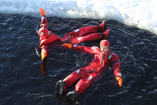 Turistas não identificados com um fato de sobrevivência nadam no mar Báltico congelado . — Fotografia de Stock