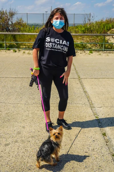 QUEENS, NEW YORK - 14 Mayıs 2020: Kadınlar Queens, New York 'taki Jacob Riis Park gezinti alanında Coronavirus salgını sırasında açık havada eğlenmek için t-kısa sosyal mesafeler katediyorlar 