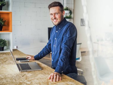 Mavi gömlekli bir adam birlikte çalıştığı ofiste dizüstü bilgisayar kullanıyor, uzaktan kumandalı internet işi ve karantina ofisi.