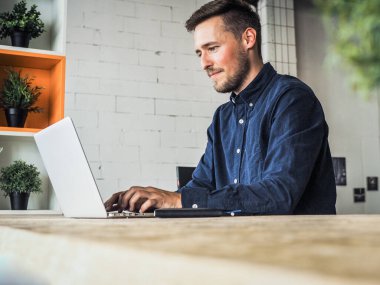 Mavi gömlekli bir adam birlikte çalıştığı ofiste dizüstü bilgisayar kullanıyor, uzaktan kumandalı internet işi ve karantina ofisi.