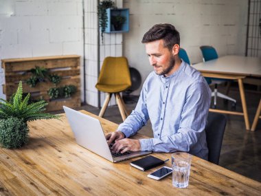 Mavi gömlekli bir adam birlikte çalıştığı ofiste dizüstü bilgisayar kullanıyor, uzaktan kumandalı internet işi ve karantina ofisi.