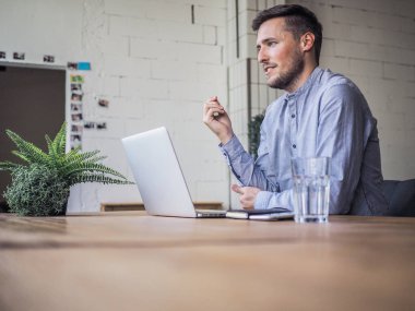 Mavi gömlekli bir adam birlikte çalıştığı ofiste dizüstü bilgisayar kullanıyor, uzaktan kumandalı internet işi ve karantina ofisi.