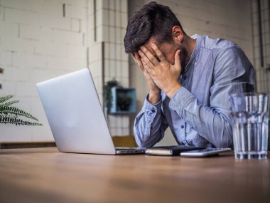 Mavi gömlekli bir adam birlikte çalıştığı ofiste dizüstü bilgisayar kullanıyor, uzaktan kumandalı internet işi ve karantina ofisi.