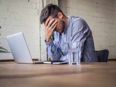 Mavi gömlekli bir adam birlikte çalıştığı ofiste dizüstü bilgisayar kullanıyor, uzaktan kumandalı internet işi ve karantina ofisi.