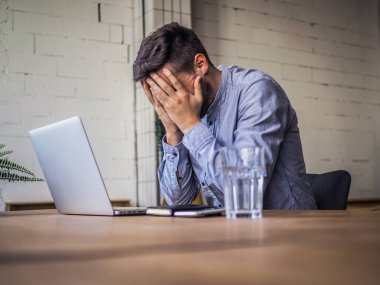 Mavi gömlekli bir adam birlikte çalıştığı ofiste dizüstü bilgisayar kullanıyor, uzaktan kumandalı internet işi ve karantina ofisi.