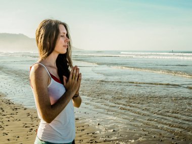 Kadın kumsalda meditasyon yapıyor.