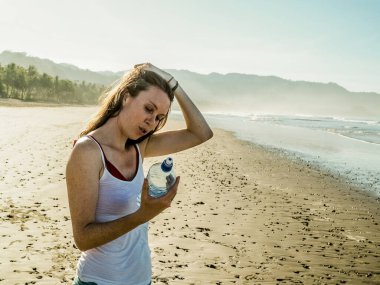 Kumsaldaki mutlu genç kadın bir şişe su içiyor. 