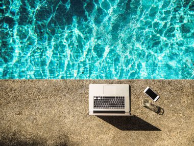 havuz başında dizüstü bilgisayar ve cep telefonu